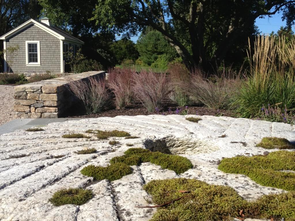 Large millstone with moss in front of ornamental grasses, Charlestown, Rhode Island