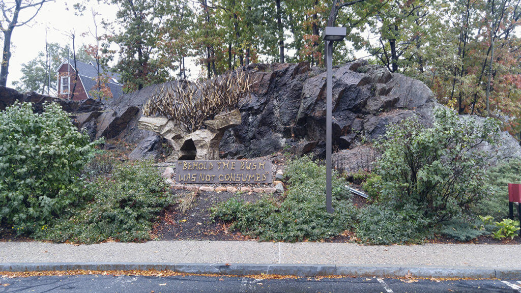 large rock feature and a sculpture of the burning bush with the quote "behold the bush was not consumed"