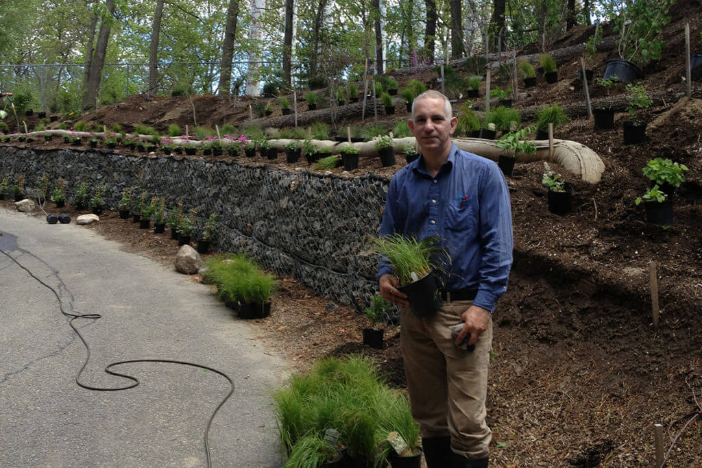 Tom Benjamin, Landscape Architect, standing in front of rock wall